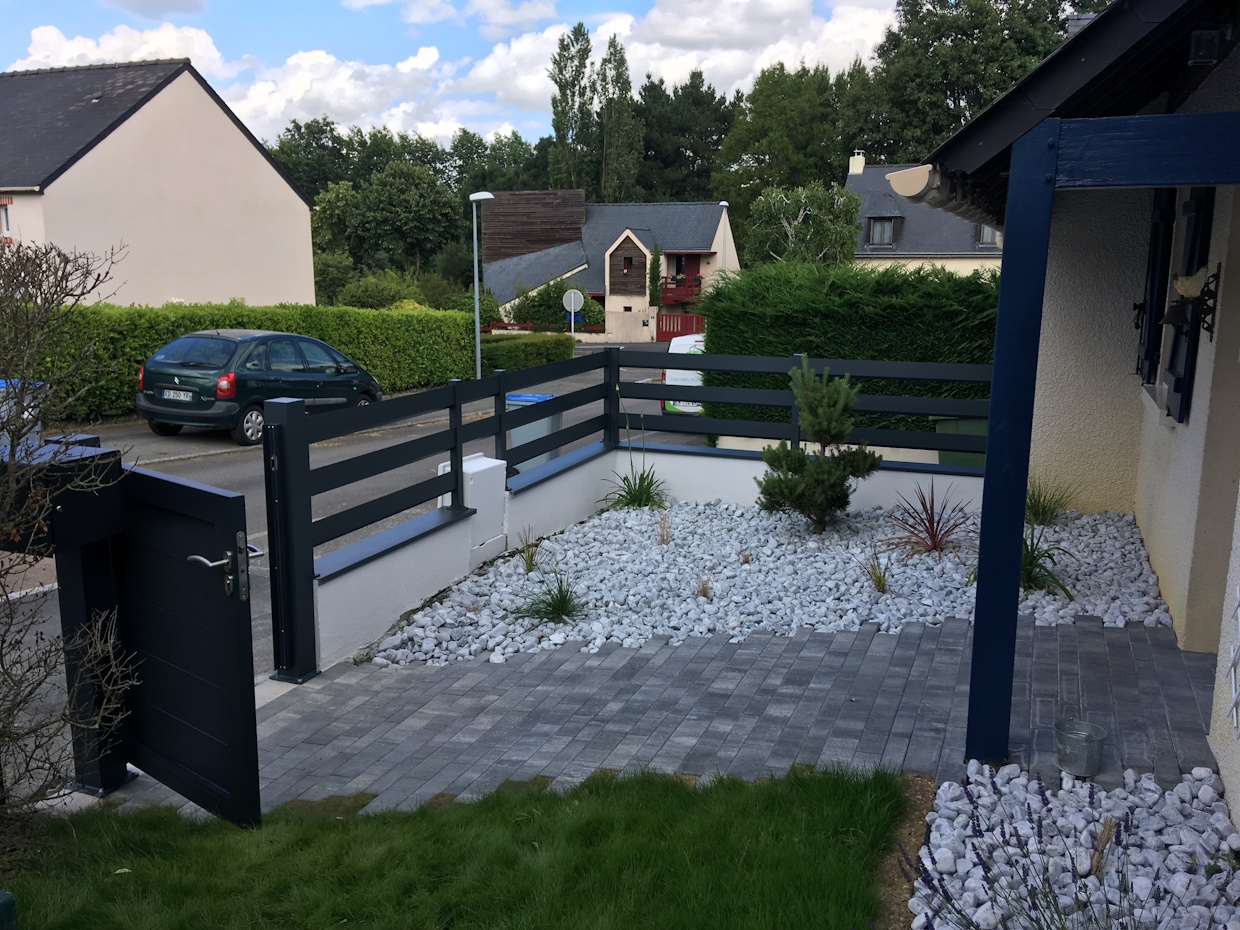 Jardin devant maison moderne avec clôture et galets.