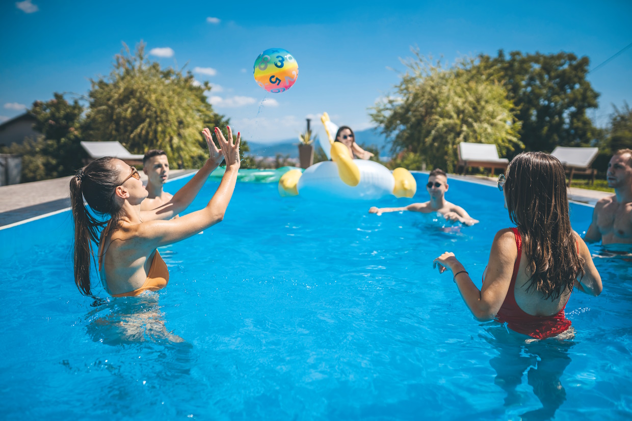 Amis jouant au ballon dans piscine ensoleillée.