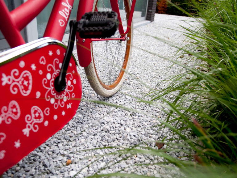 Vélo rouge avec panier décoratif sur gravier.