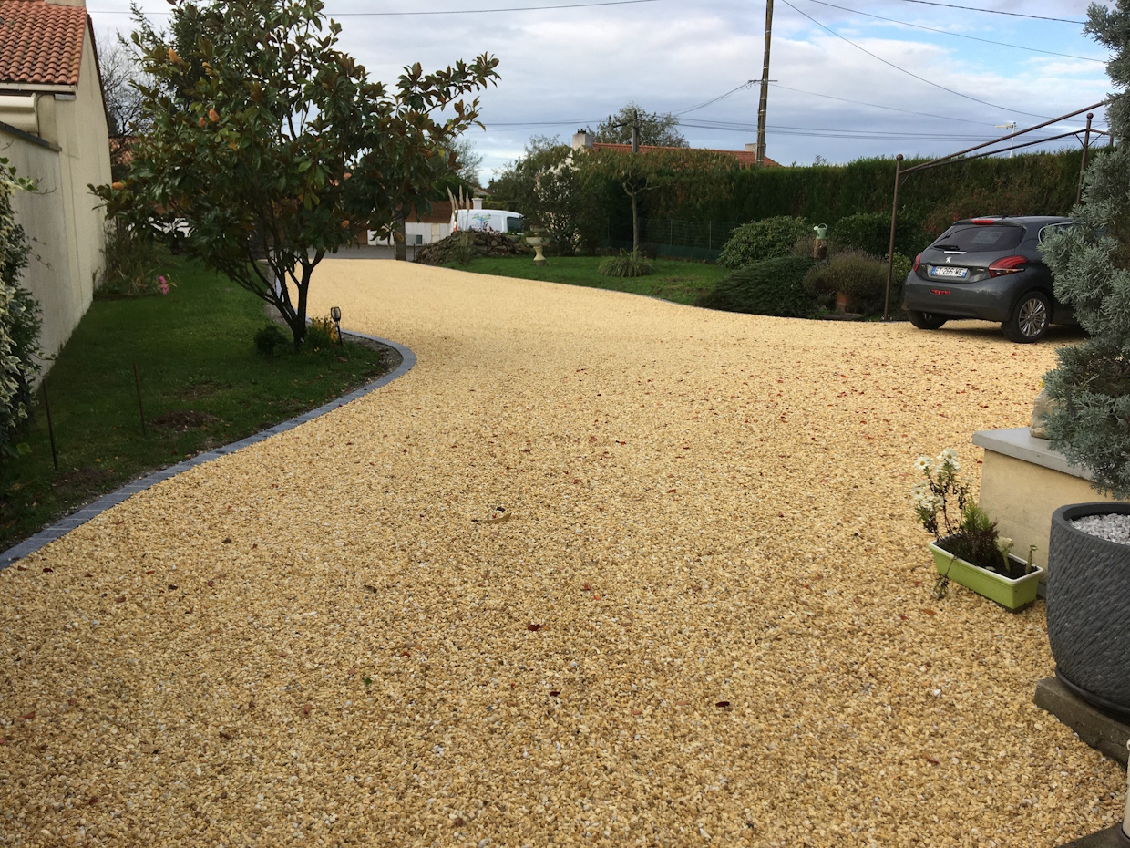 Allée gravillonnée avec voiture et jardin verdoyant.