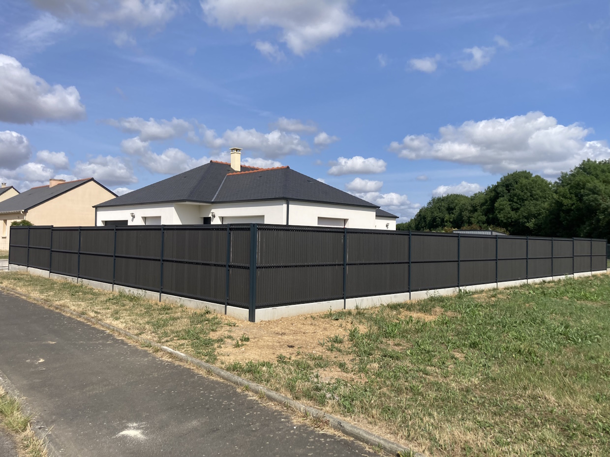 Maison moderne avec clôture noire et ciel nuageux.