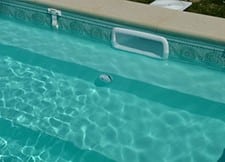 Piscine d'eau claire avec échelle et ballon flottant.