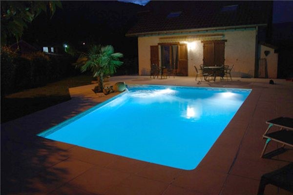 Piscine éclairée la nuit, maison familiale.