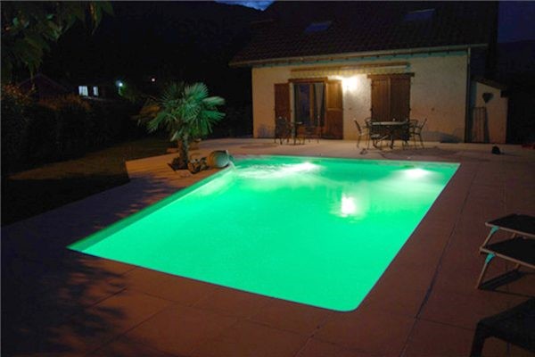 Piscine éclairée nocturne, maison moderne, jardin.
