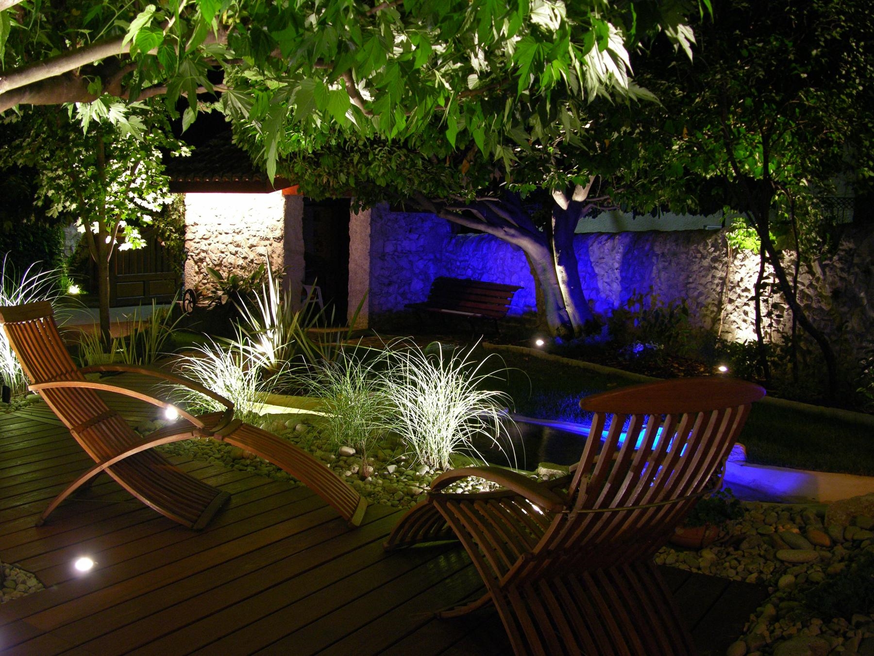Jardin éclairé de nuit, chaises longues, ambiance zen.