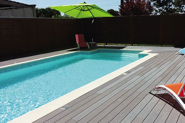 Piscine extérieure ensoleillée avec parasol et chaises longues.