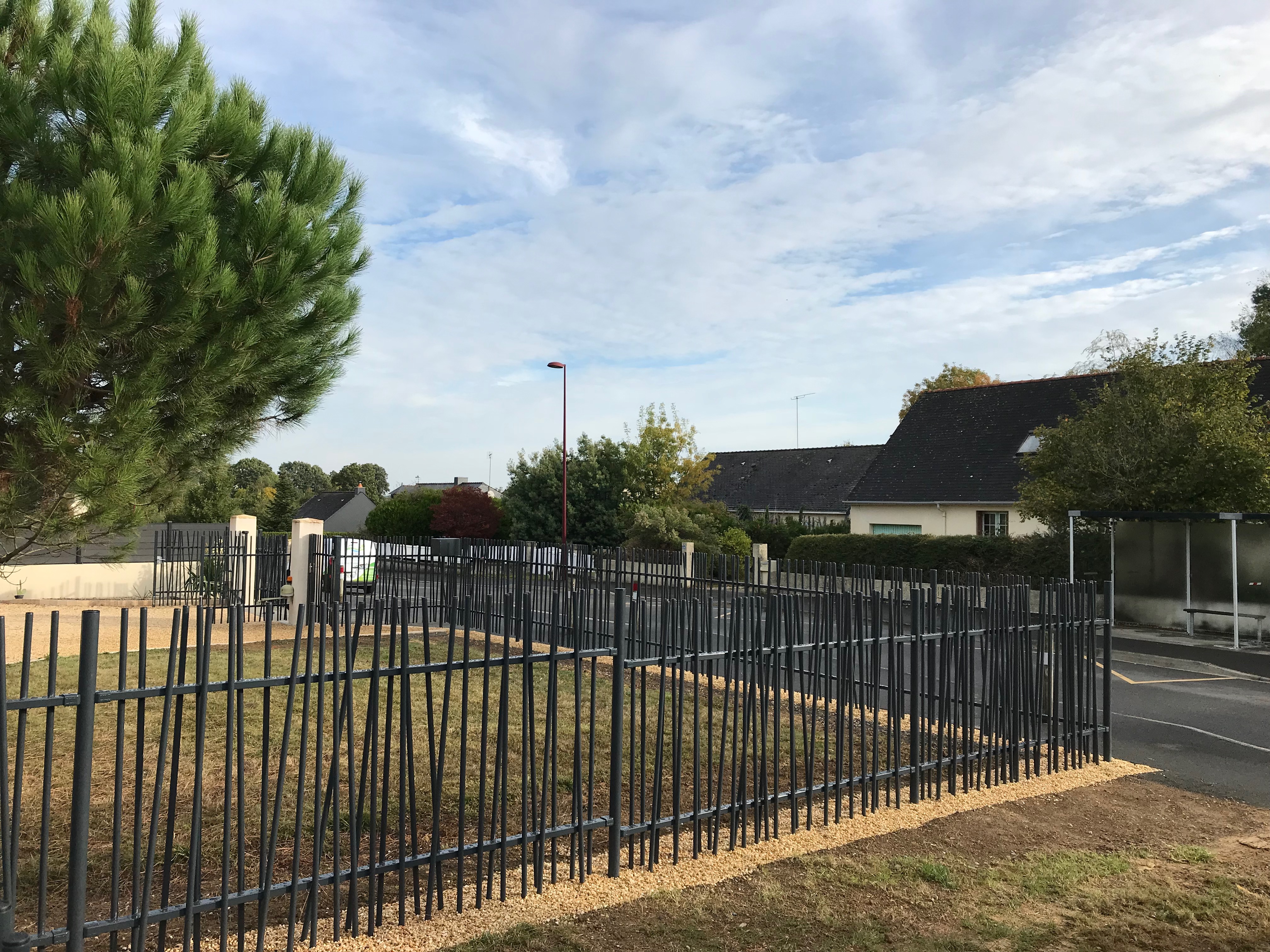 Parc urbain, clôture métallique, arbres, ciel nuageux