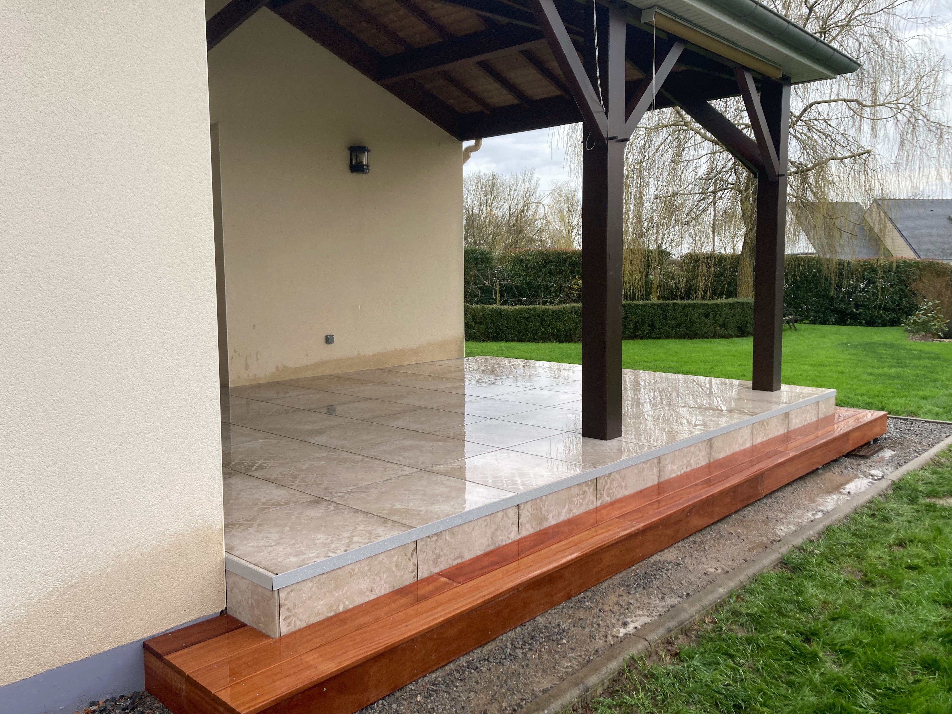 Terrasse carrelée extérieure avec pergola en bois.