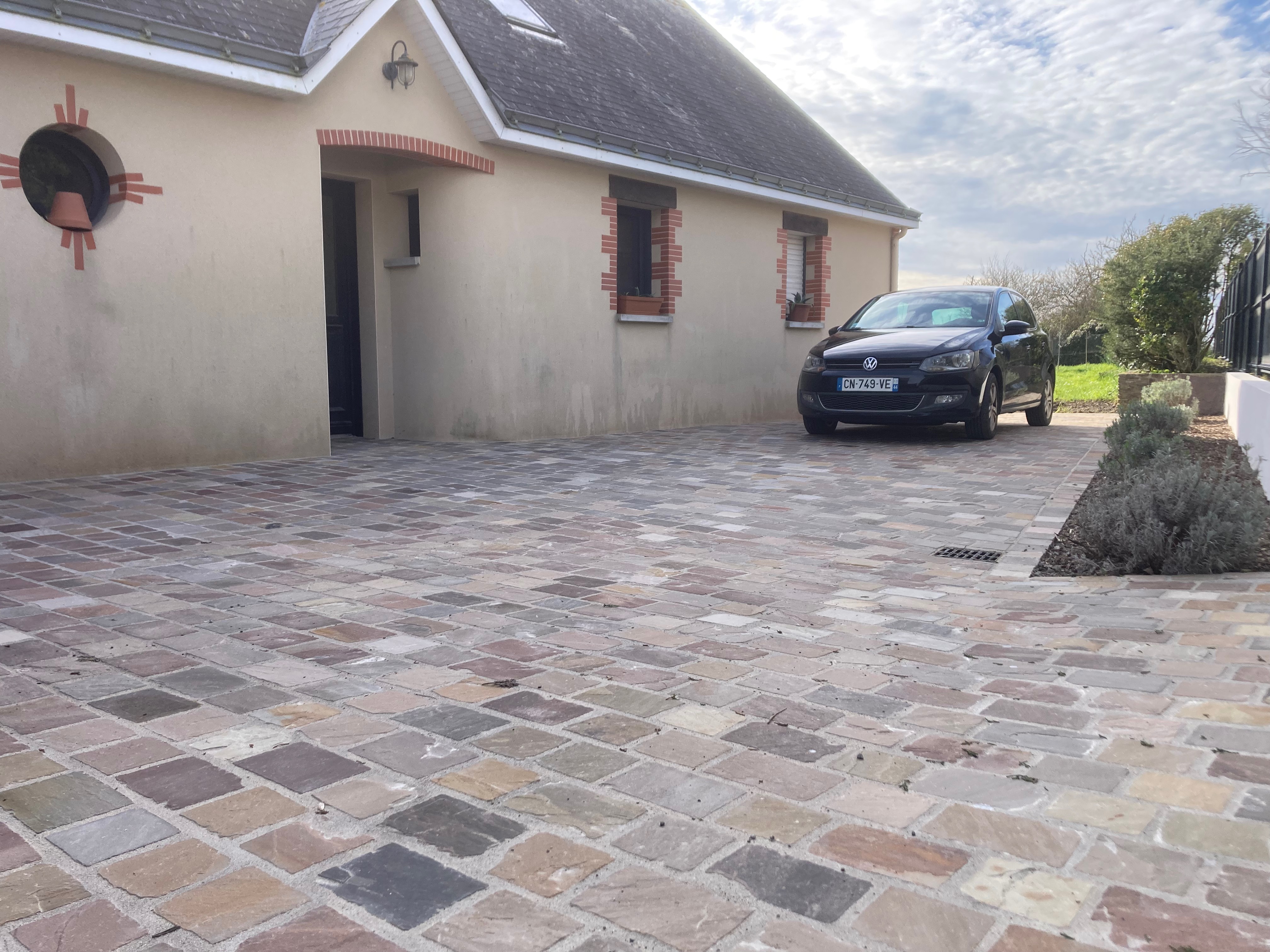Maison avec allée pavée et voiture noire stationnée.